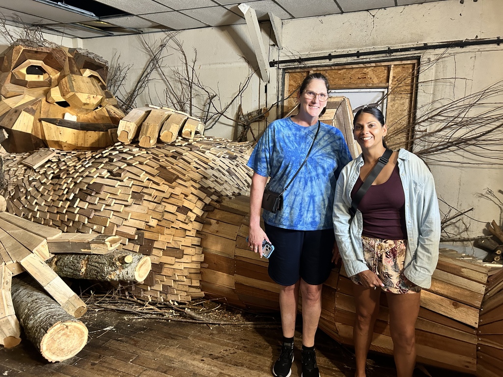 Nicole & Stacey take a selfie with a troll sleeping in a room.