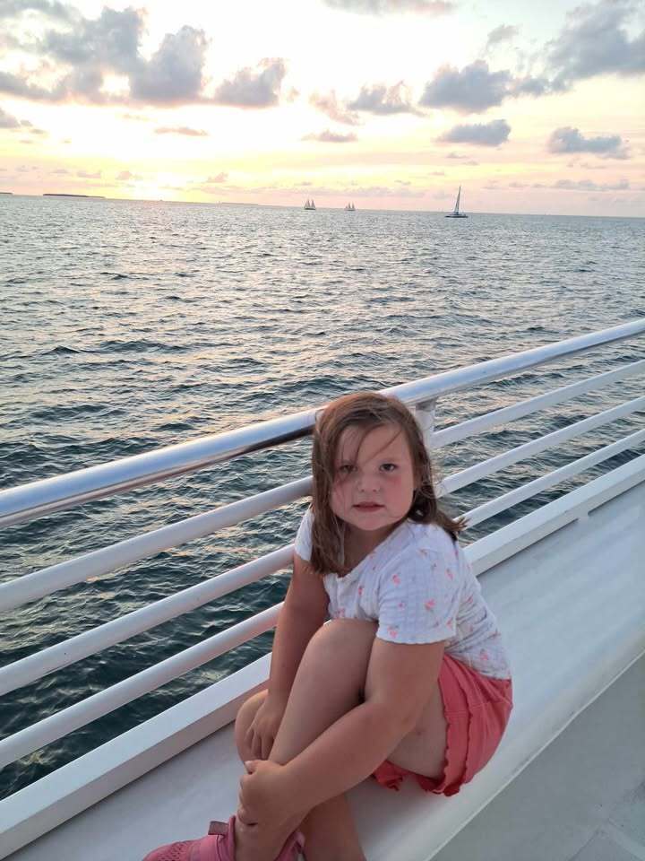 Lydia sitting by the rail on a boat during sunset