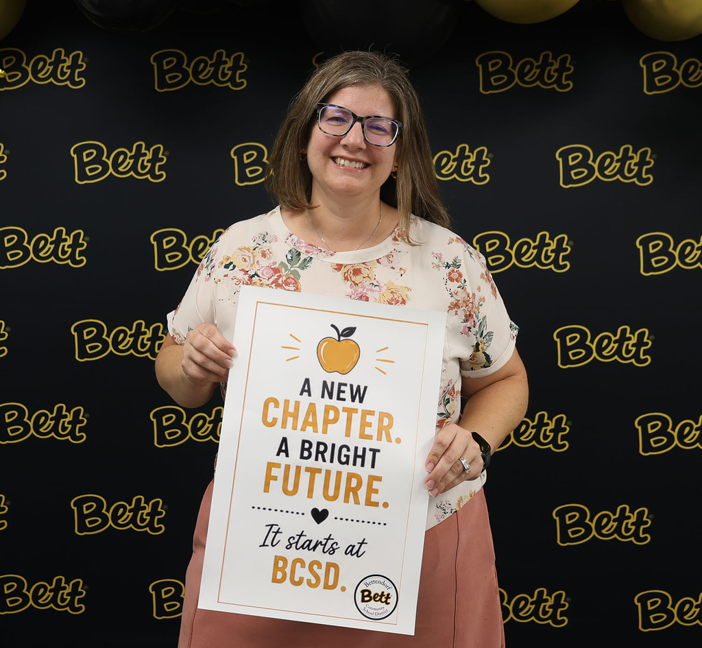 Nicole Kelso holding a sign - A new chapter. A bright future. It all starts at BCSD. Bettendorf Community School District Logo
