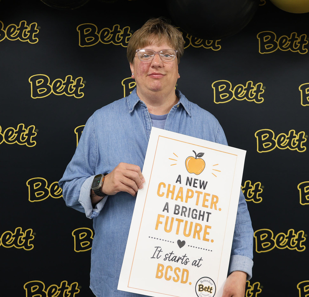 Theresa Moneymaker holding a sign - A new chapter. A bright future. It all starts at BCSD. Bettendorf Community School District Logo