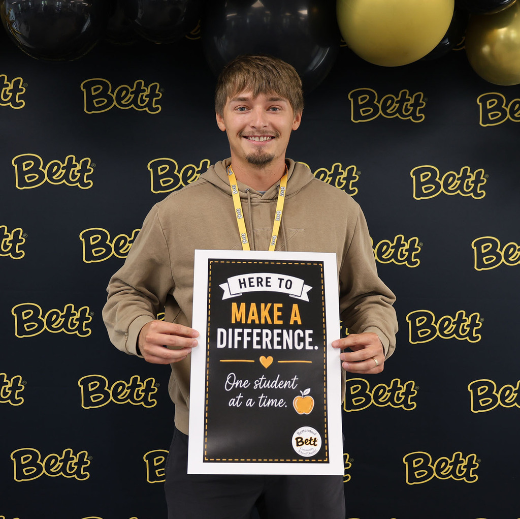 Alex Heiman with a sign: Here to make a difference. Heart. One Student at a time. apple. Bettendorf Community School District logo with Bett graphic