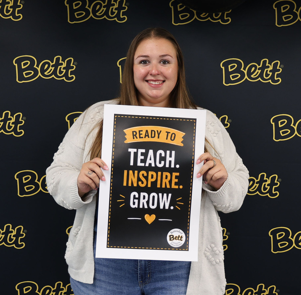 Chole Wojtowicz with a sign: Ready to teach. Ispire. Grow. heart. Bettendorf Community School District logo with Bett graphic
