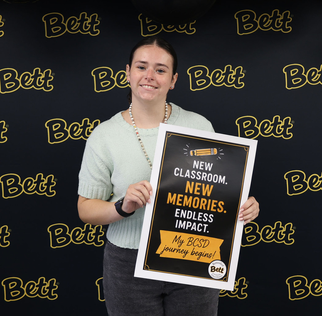 Andrea Daley with a sign: New classroom. New memories. Endless impact. My BCSD journey begins.Bettendorf Community School District logo with Bett graphic