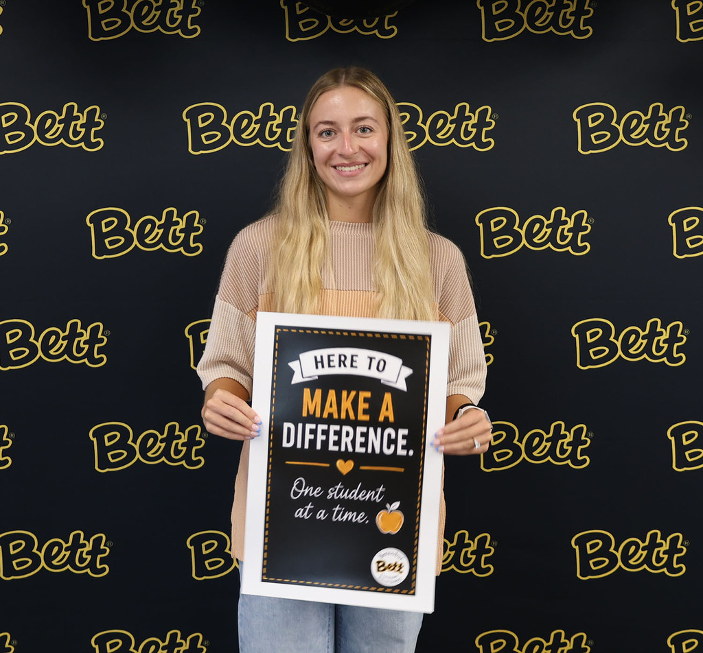 Lauryne Pearson BMS holding a sign: Here to make a difference. Heart. One student at a time. Apple.  Bettendorf Community School District logo with Bett graphic.