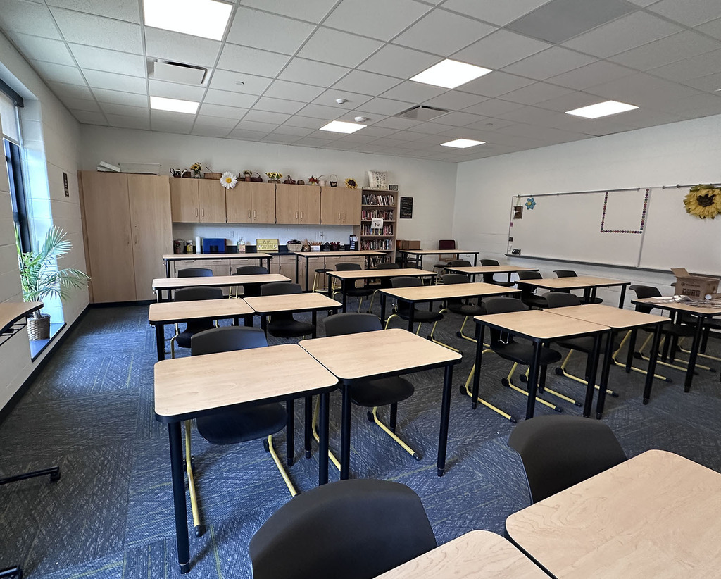 A classroom with student desks and chairs some daiseies and cabinets