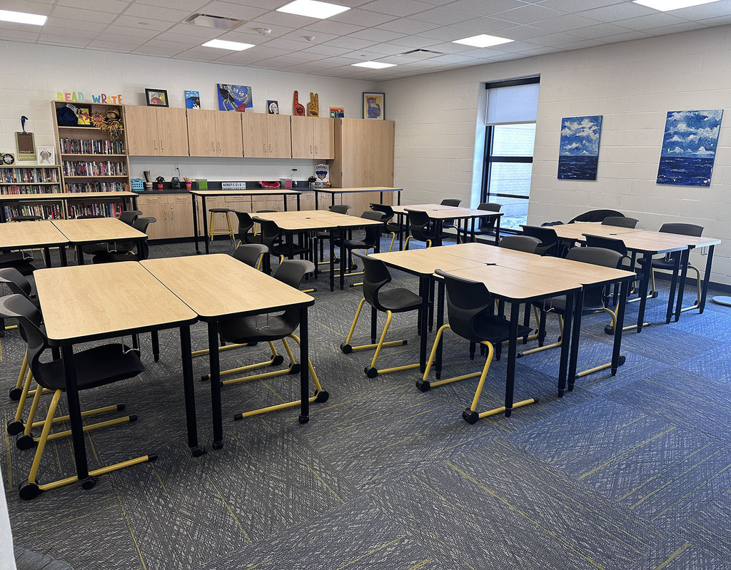 A classroom with desks and chairs. Blue artwork on the wall. A book shelved loading with books.