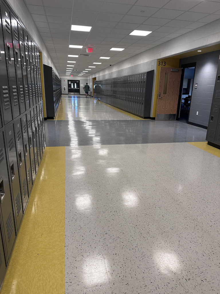 A yellow and shades of grey hallway with banks of lockers on the wall and classroom doorways in bright yellow.