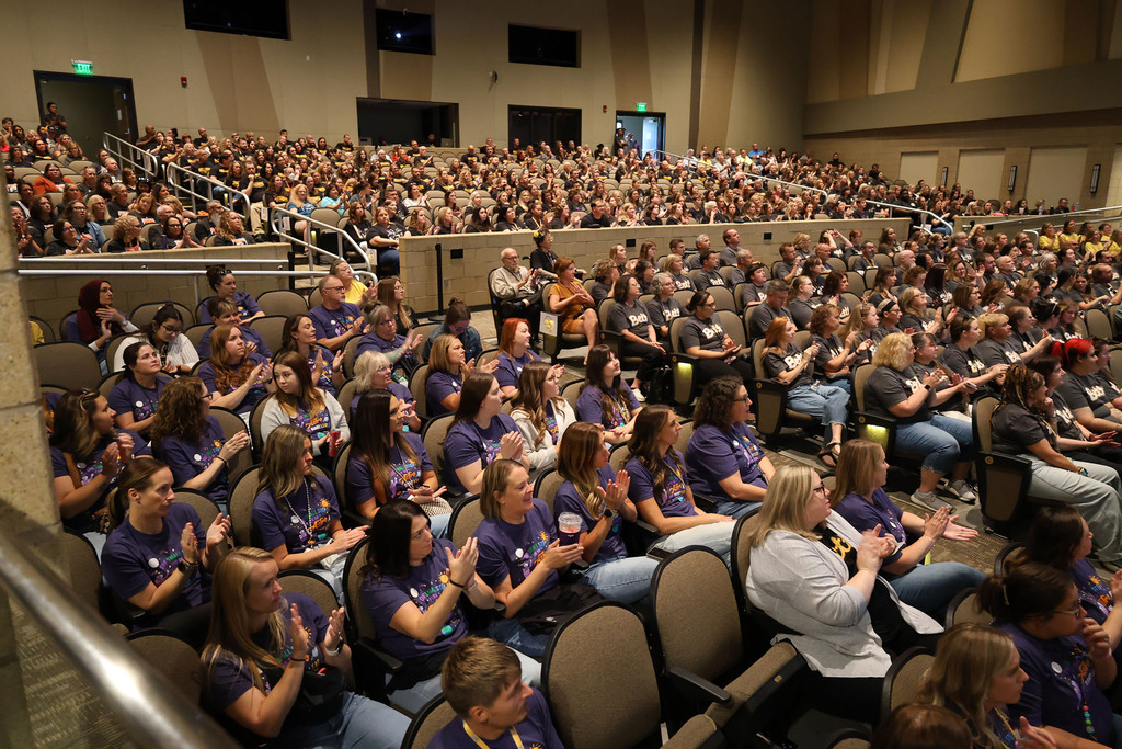 A pisture of the staff sitting in ther school section applauding.
