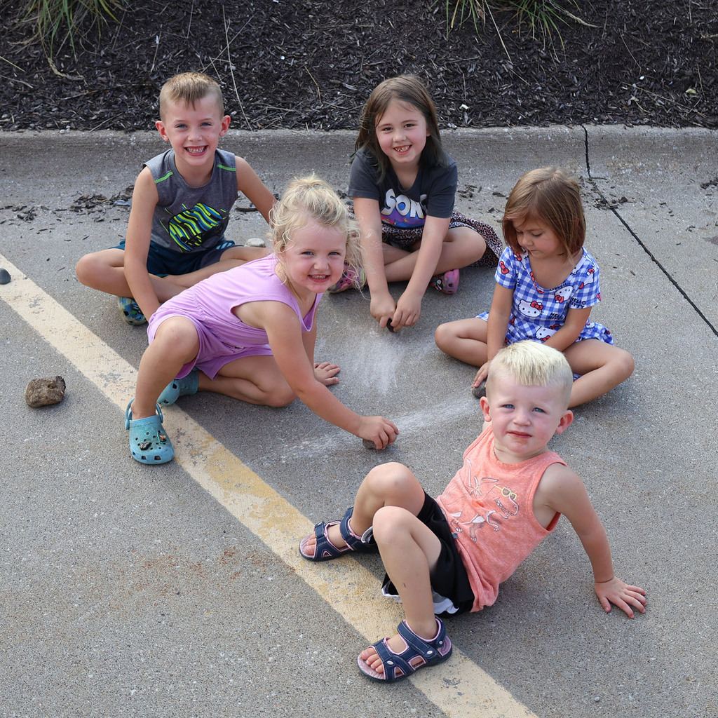 Five adorable young kids drawing on the parking lot with rocks waiting for the Knights Pizz line.
