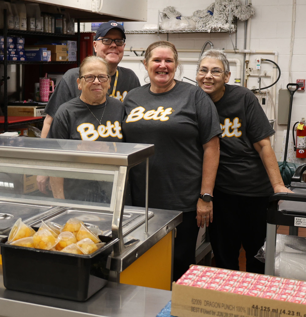 Bettendorf Middle School nutrition services staff gathered for a picture in the grey shirts with the Bett logo behind the counter.