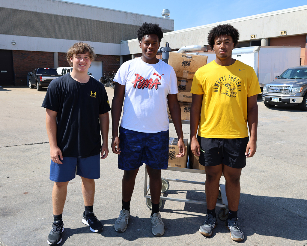 Three football players with a cart of food for the trailer