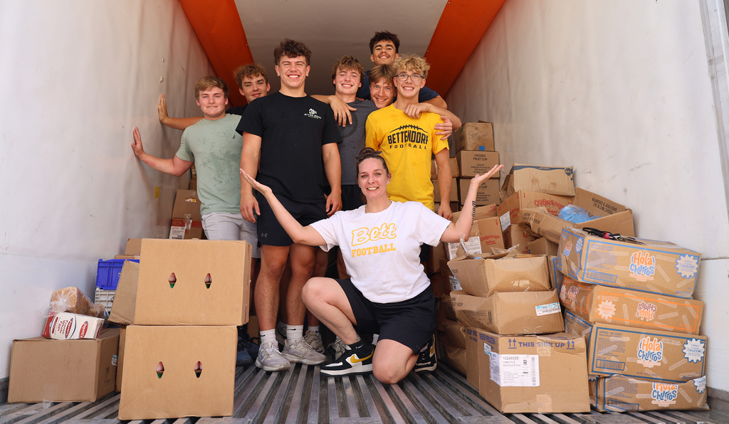 Football players and coach who help sort the food in the freezer trailer.