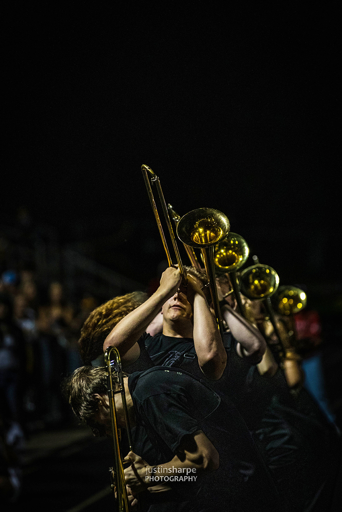 Trombone players in a line playing during a night football game