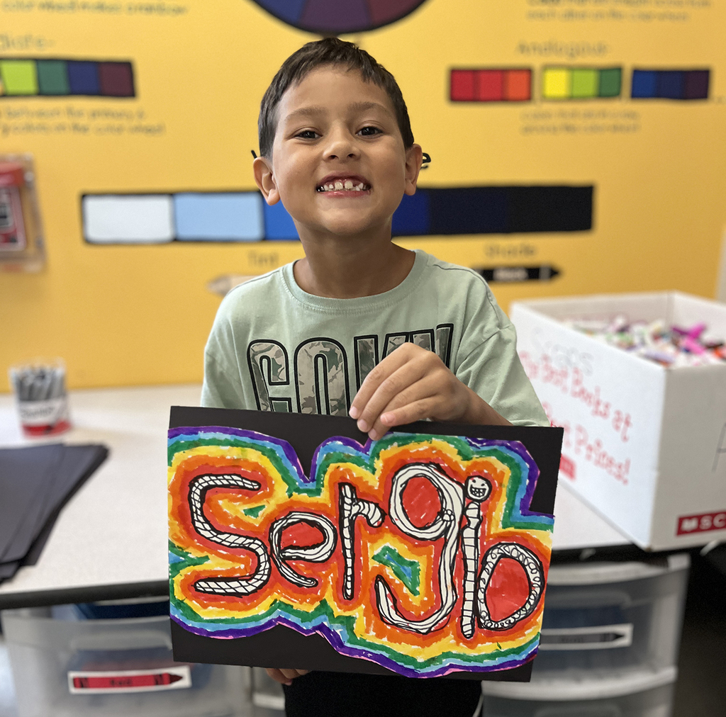 Sergio smiling with his art design in black, white, orange, yellow, green, blue, and purple