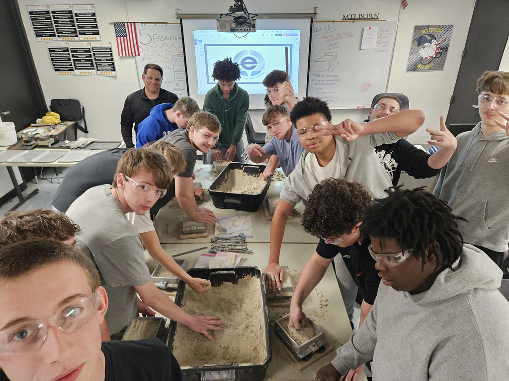 Students taking a selfie of the group by a table with the containers of sand