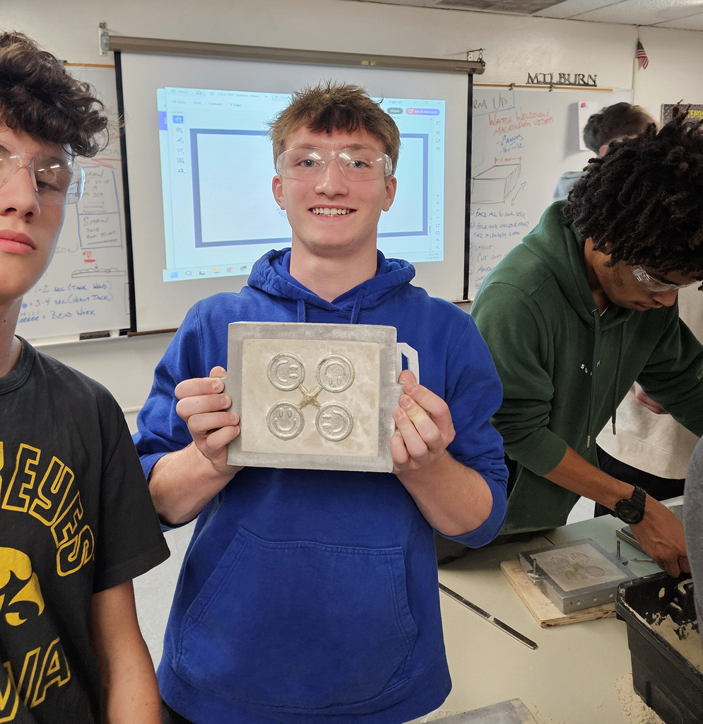 Student showing his metal casting of 4 smilely faces connected with an X
