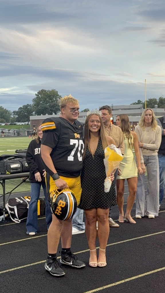 Gavin Barr in his football uniform with Katelyn Fritz with a crown and holding a boquet of flowers.