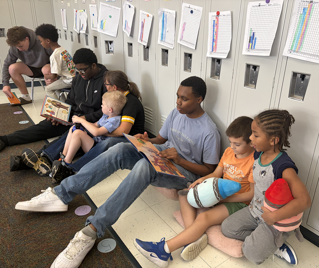 Students lined up on the floor in front of lockers with the HS students reading to small sets of elem students