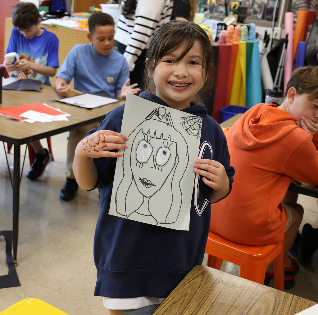 A girl holding her spooky self portrait with a spider on the top of her head