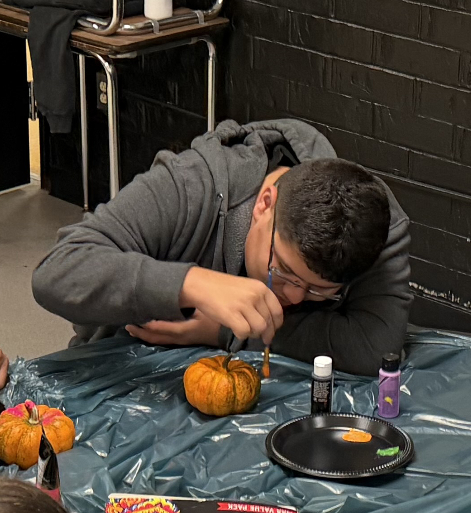 Student huddled over pumkin with a paint brush