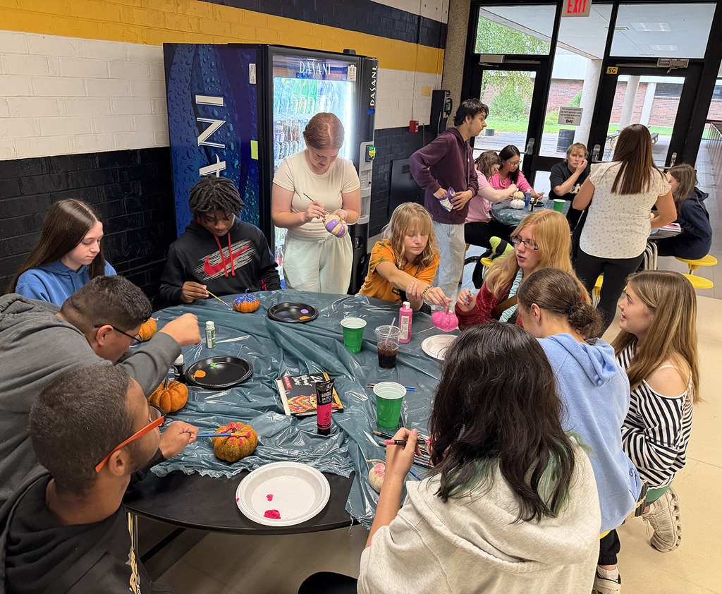 Two tables of students working on painting pumpkins