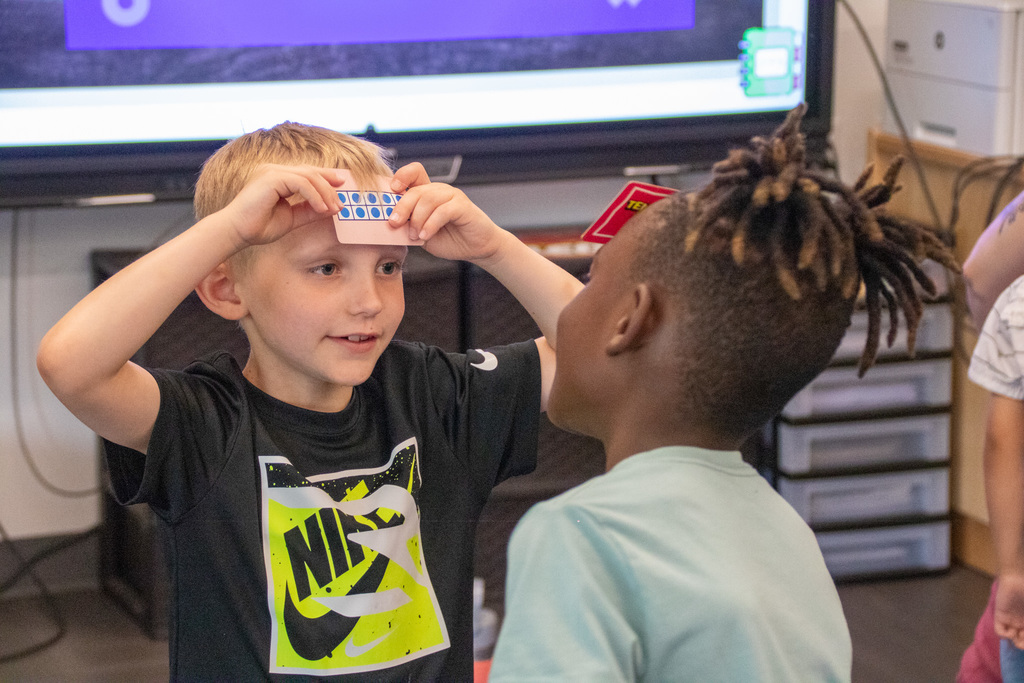 student tries to guess the number of dots on the card he holds against his forehead while another student gives clues