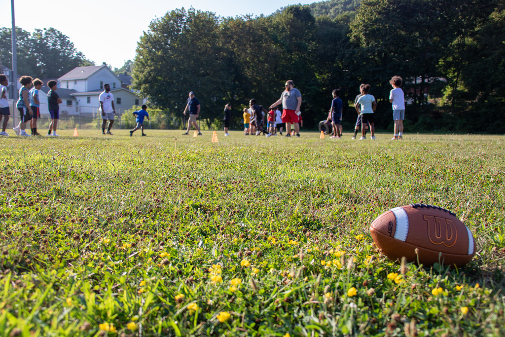 photo of football laying on ground with students practicing in background