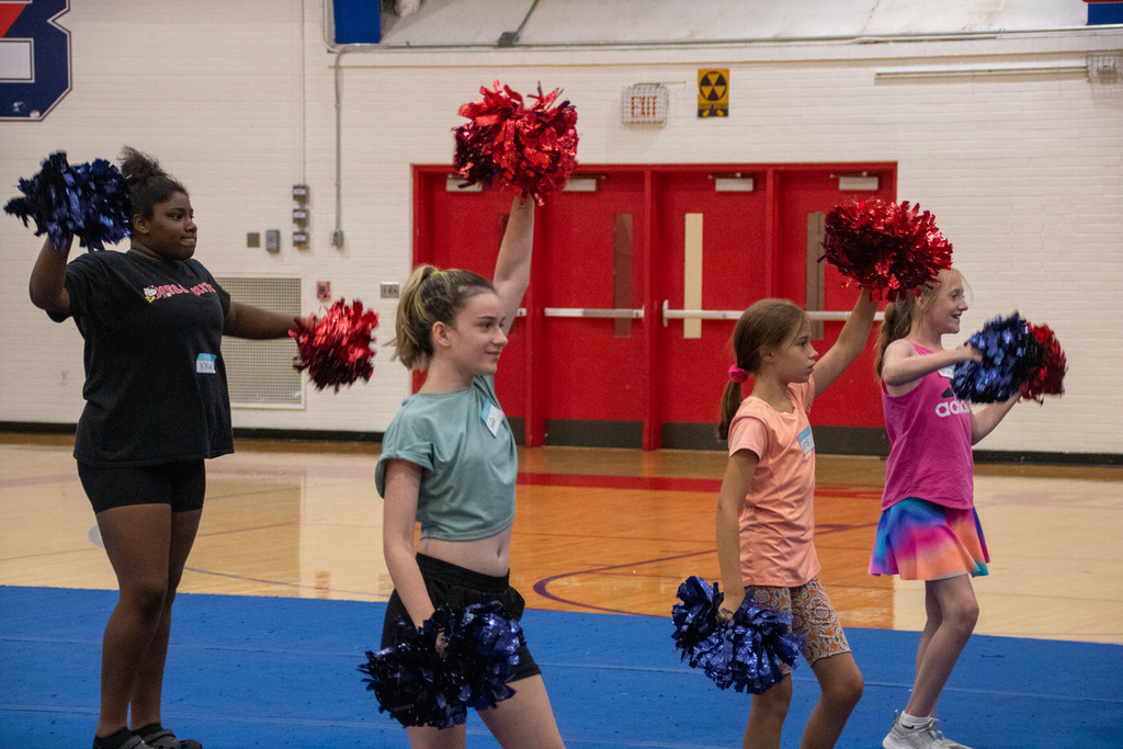 students hold pom poms up in the air during Patriots cheer camp
