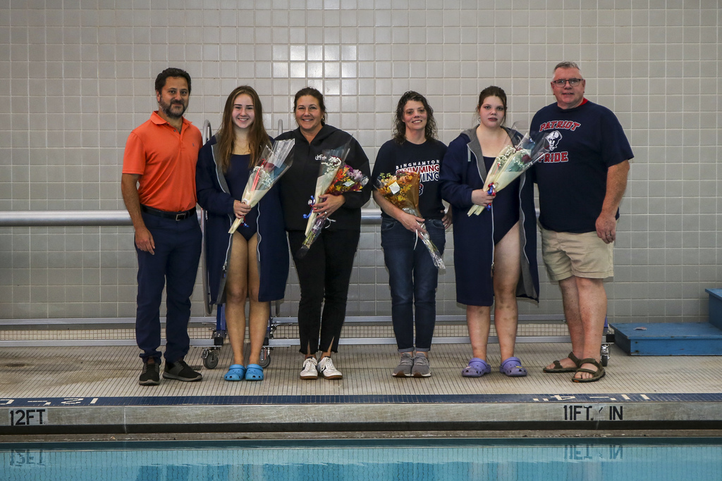 seniors from the girls swim team pose for photo with their parents while holding flowers