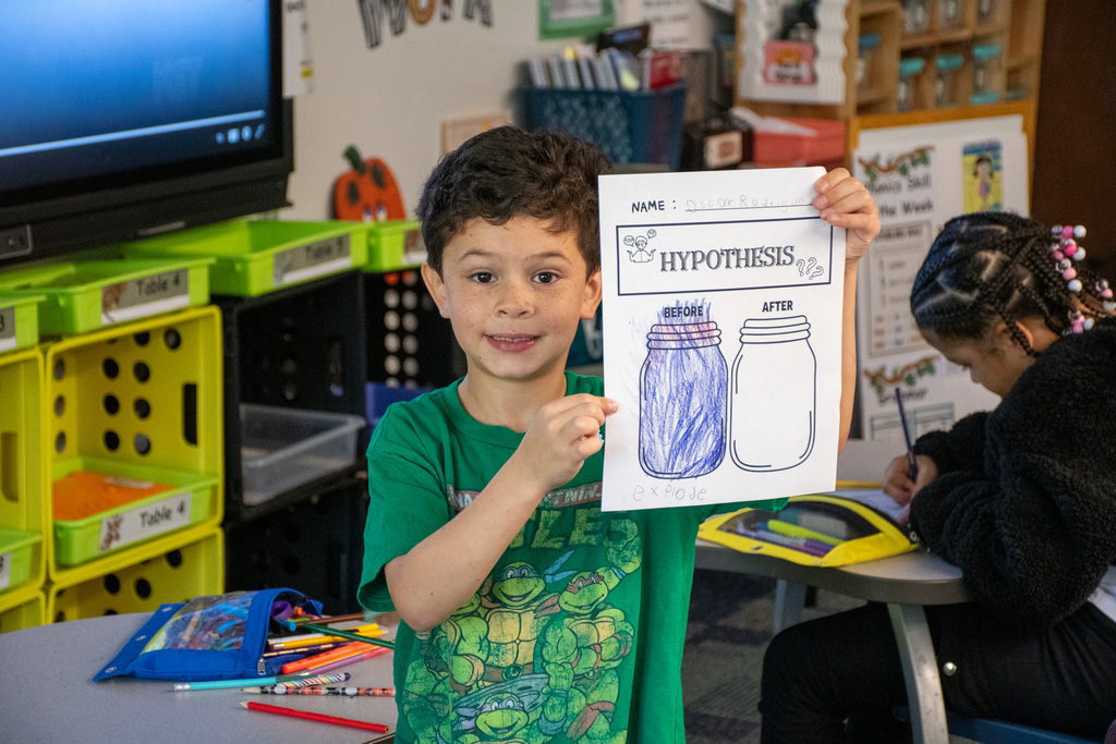student holds up a paper with his hypothesis on it