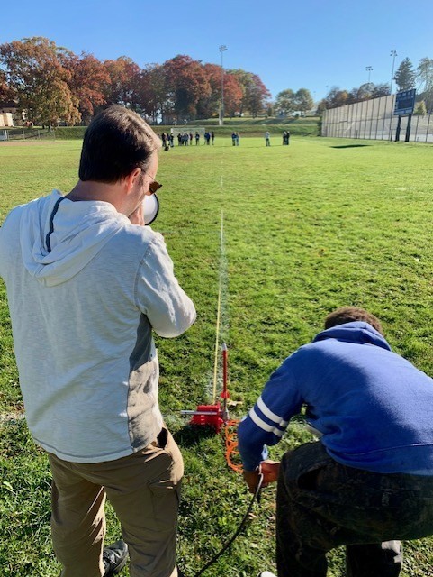 physics teacher instructs student as he launches rocket at recreation park