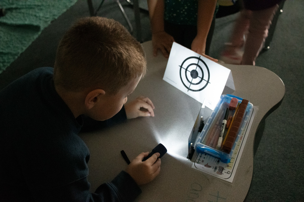 student uses mirror to shine light onto a paper card