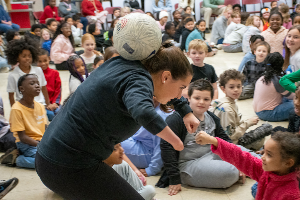 alexia michitti balances soccer ball behind her head and gives fist bump to student