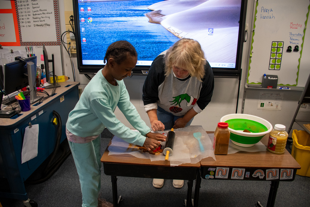 teacher helps student cut out shape from dough