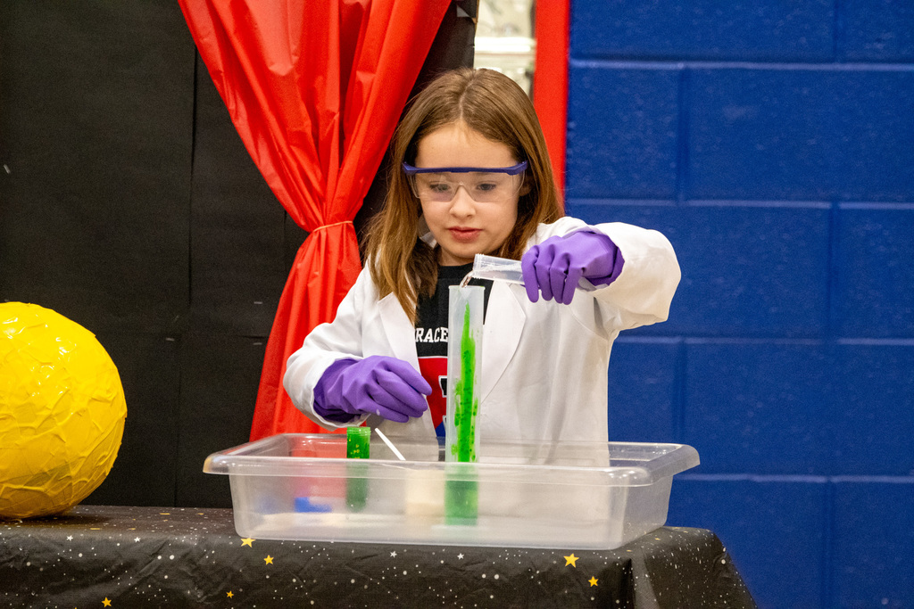 horace mann second grade student fills graduated cylinder with hydrogen peroxide while wearing lab coat, rubber gloves, and protective glasses