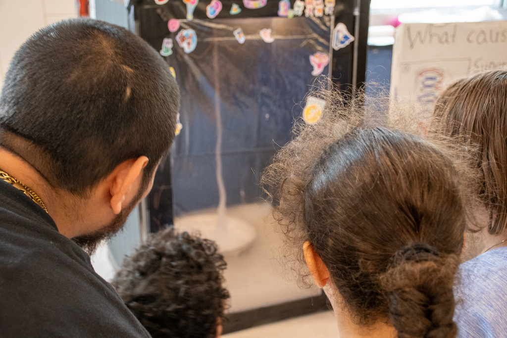 students and parent look at homemade tornado in a box