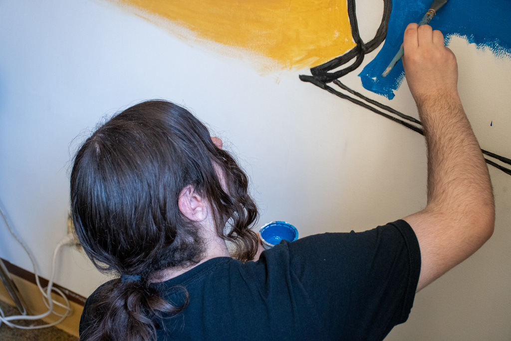 student paints portion of mural on classroom wall