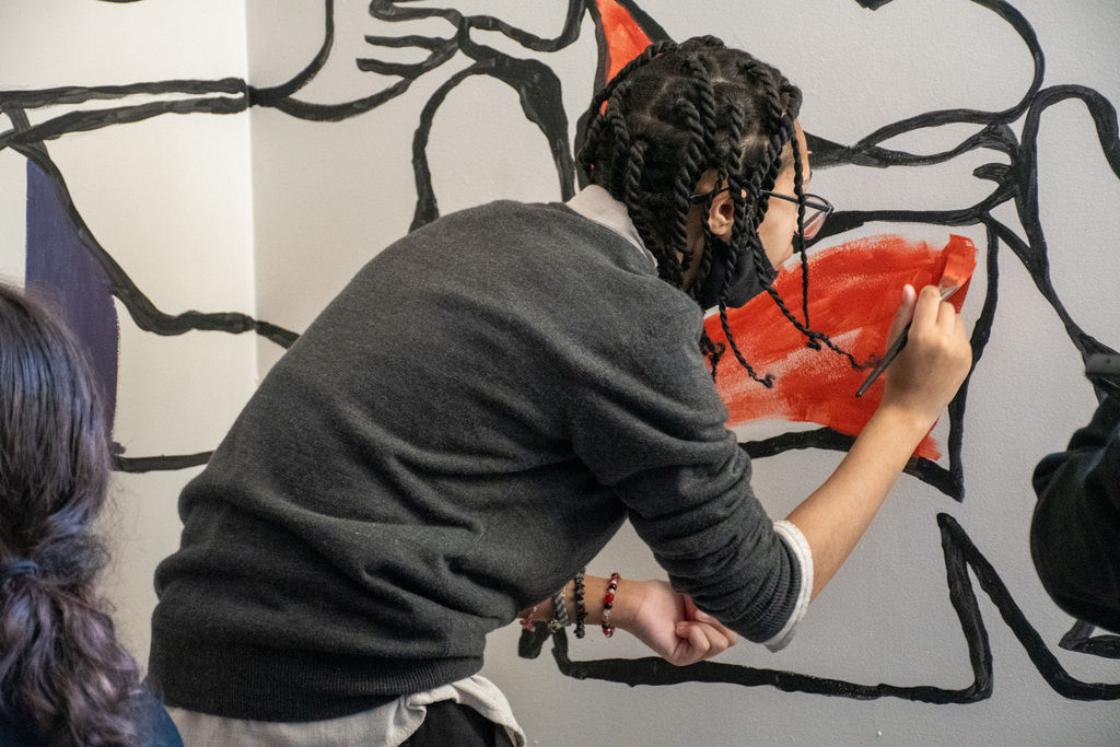 student paints a section of a classroom wall mural