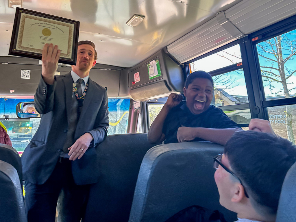 band teacher andrew garrett holds up golden award earned by franklin and roosevelt students at nyssma major organization festival
