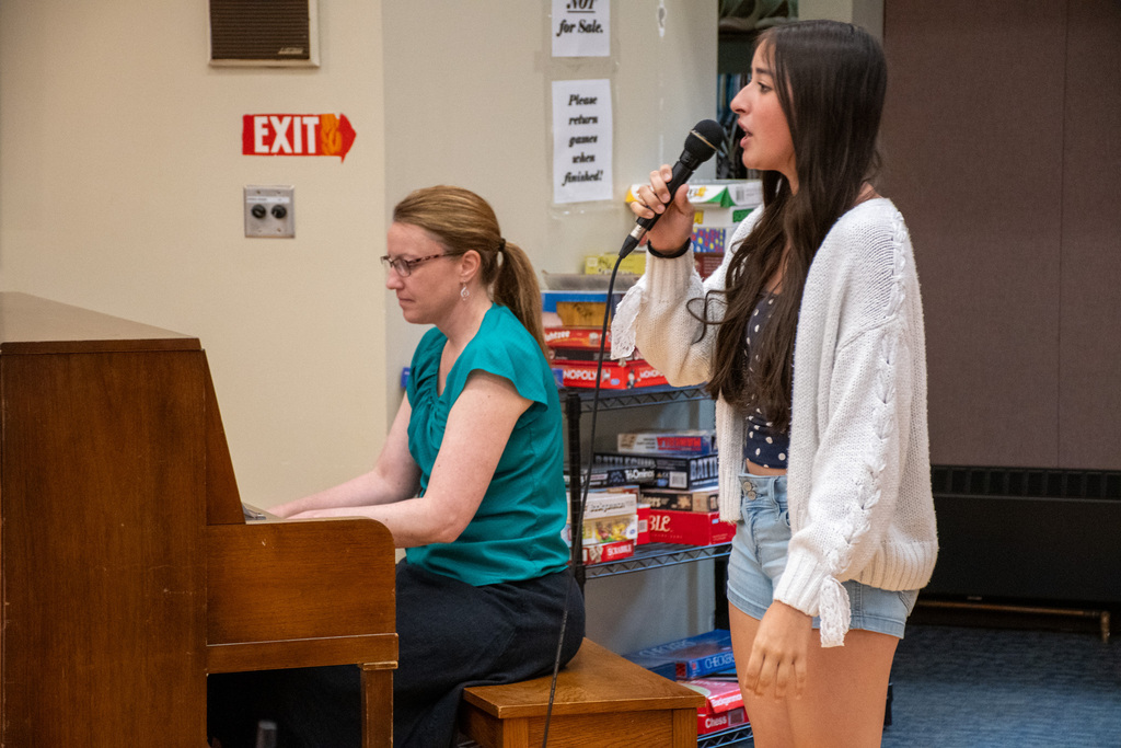student sings into microphone while teacher plays piano