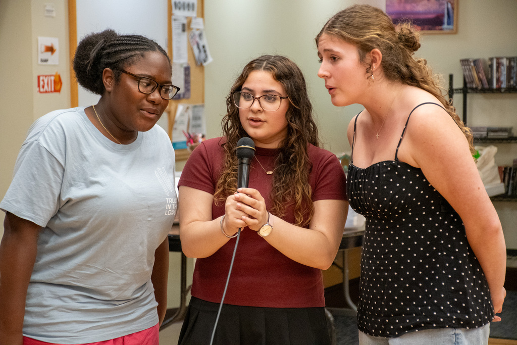 three students sing into microphone