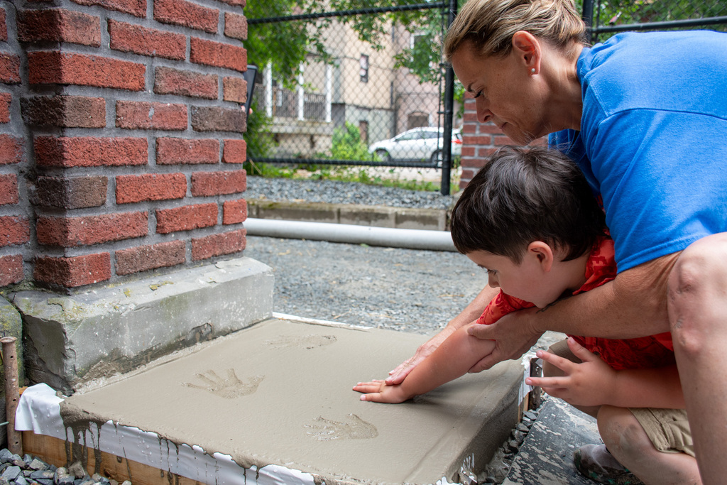 pre k teacher michelle zaverton helps her student gio marcello make a handprint in concrete