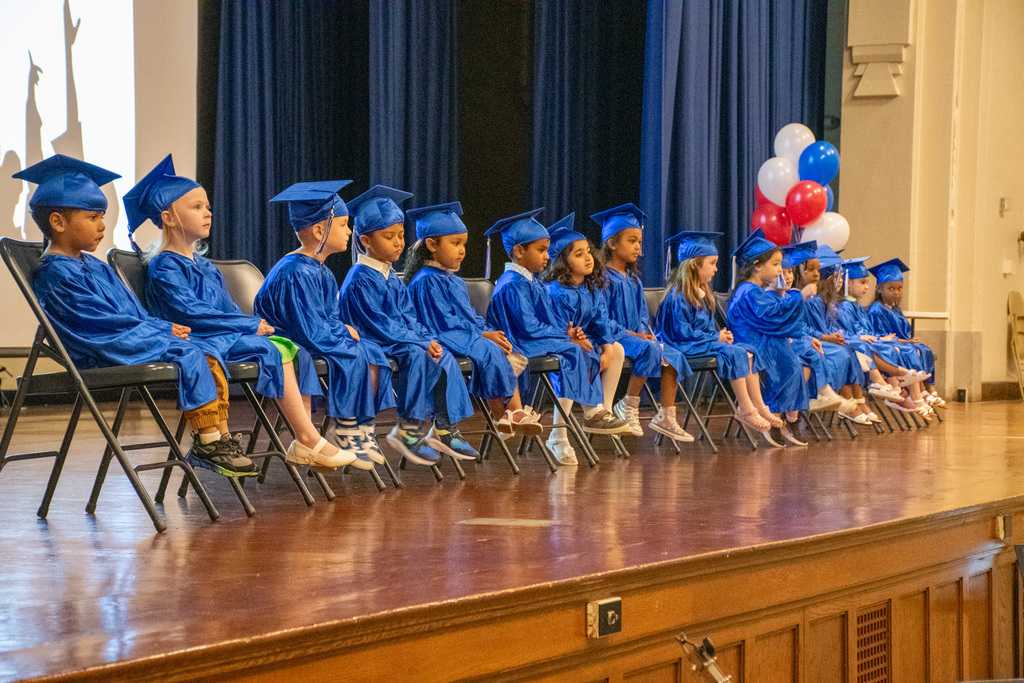 west middle school pre k students wearing blue caps and gowns sit on stage at pre k graduation