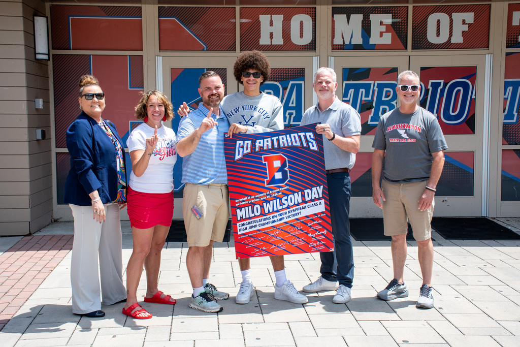 milo wilson with coaches and county officials holding banner proclaiming milo wilson day in broome county