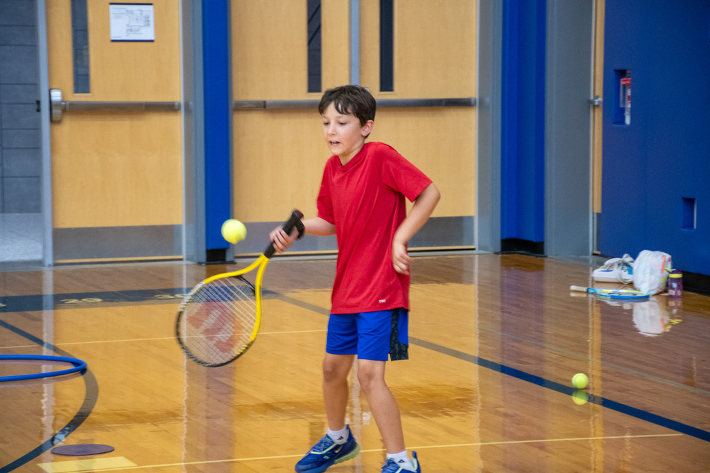 student swings tennis racket to hit ball