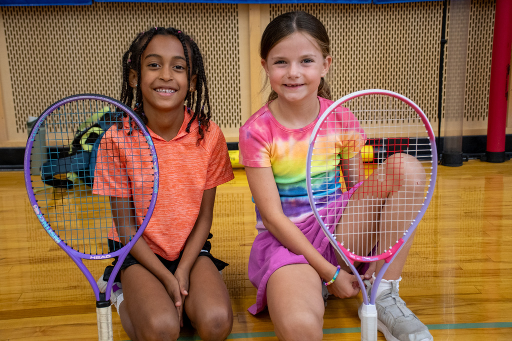 two students smile for camera with tennis rackets standing on gym floor