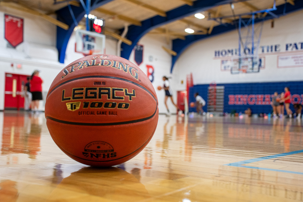 basketball on gym floor with girls playing basketball in background