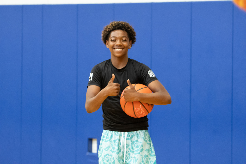 student gives two thumbs up while holding basketball underneath arm