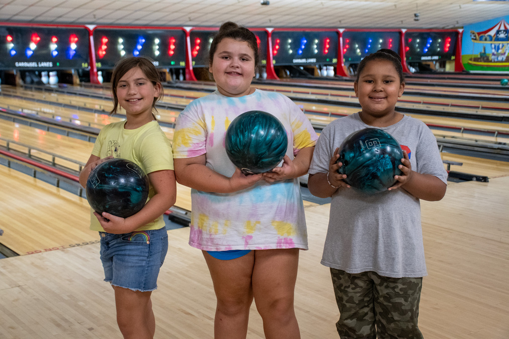 three students hold bowling balls at patriots bowling camp