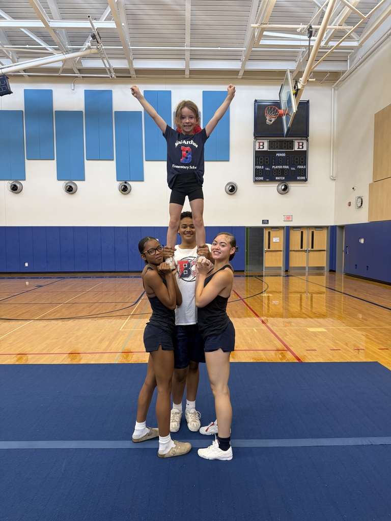 three high school cheerleaders hold elementary student's ankles as she stands in a cheer pyramid